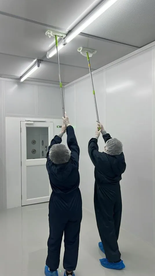 Technicians cleaning a cleanroom ceiling in full PPE