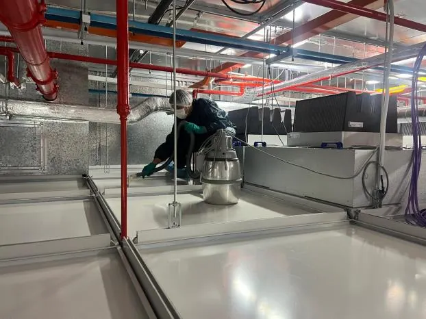 Technician servicing HVAC ductwork in the ceiling plenum in PPE